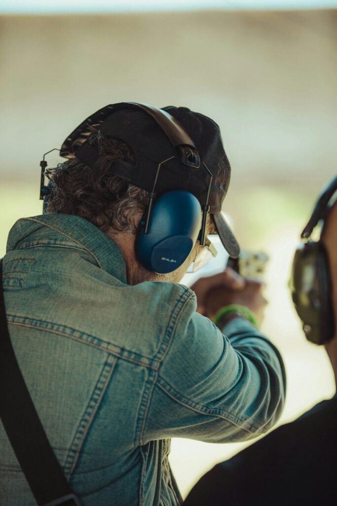 Two adults practicing shooting outdoors with protective gear.